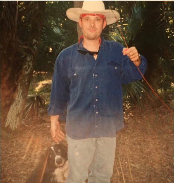 Steve Coder, founder of Hand to the Plow Ministries, holding a stick outdoors with Levi the Wonderdog beside him