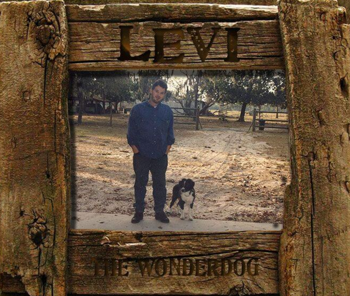 An image in a wooden frame displaying Steve Coder, founder of Hand to the Plow Ministries, standing in a driveway beside Levi the Wonderdog