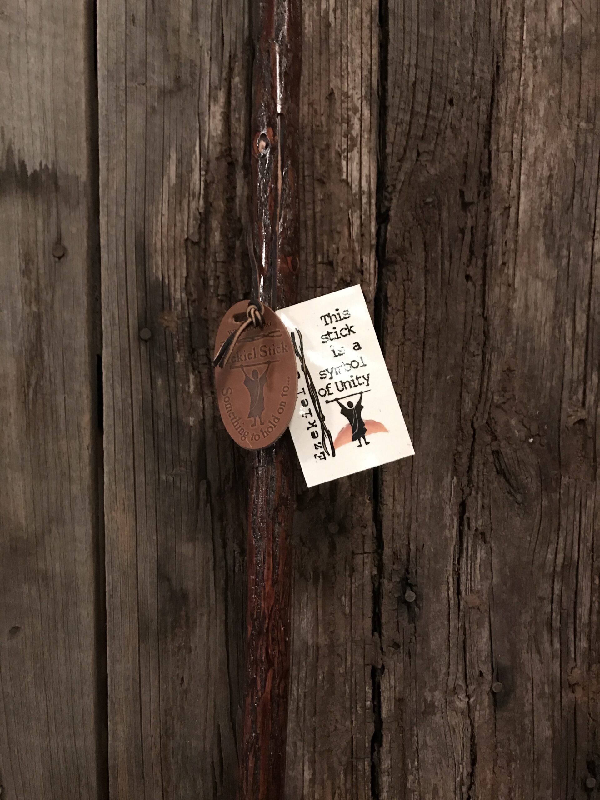 Walking stick with Ezekiel Stick card attached, photographed against rustic barn wood background
